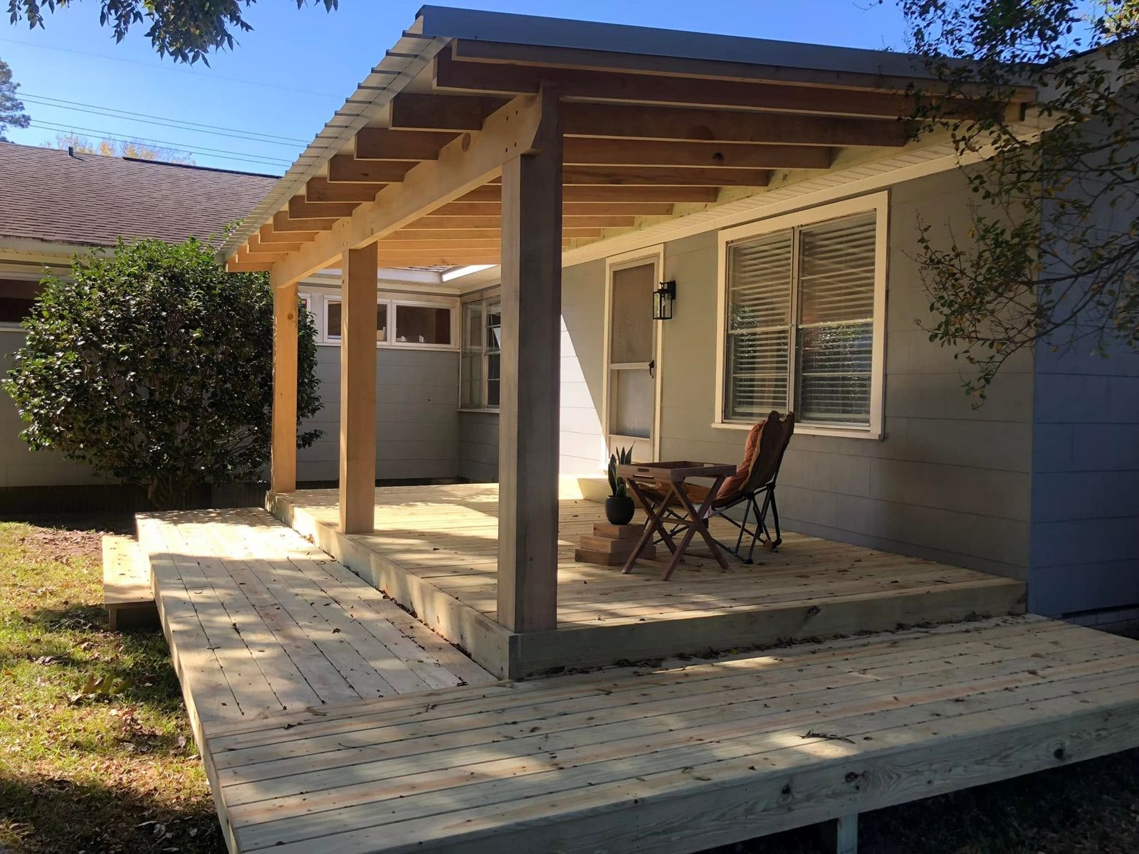 New covered deck with timber posts and exposed rafters on a gray house